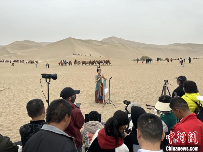 圖為2023年4月底，敦煌大漠“逐舞者”奧楠在鳴沙山月牙泉景區(qū)視頻直播，吸引游人圍觀。　馮志軍 攝